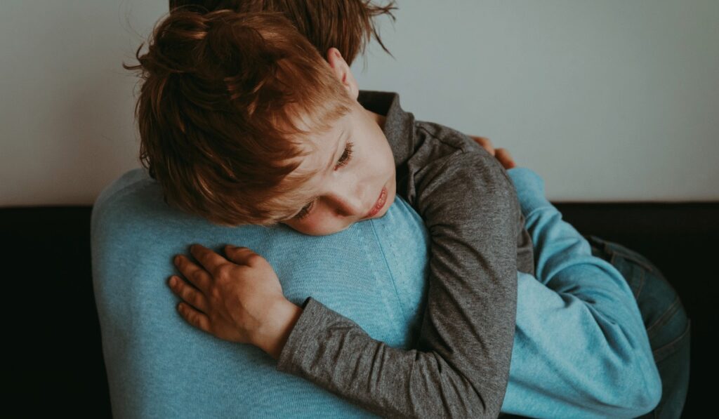 Eine Mutter umarmt ein traurig wirkendes Kind 