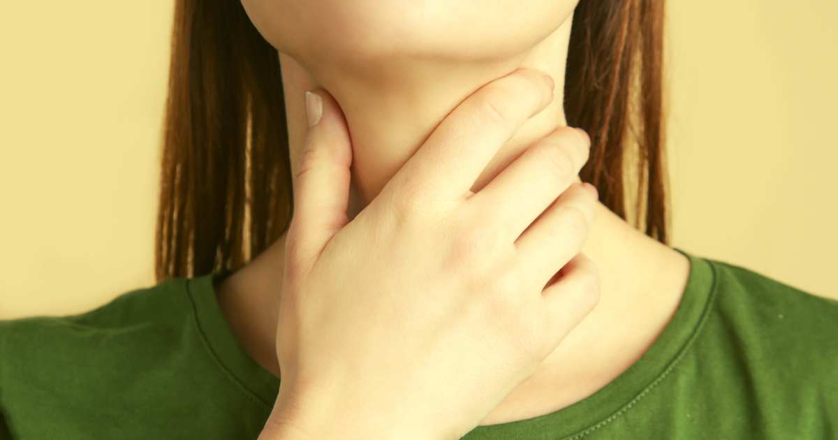 Heiserkeit ist unangenehm. Eine Frau fasst an ihren Hals in der Höhe der Stimme bzw. des Kehlkopfes.