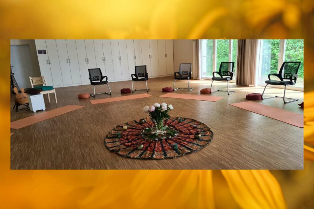 Eine Mitte für einen Singkreis bestehend aus einem runden Tuch mit Mandala-Muster, Teelichten und einem Blumenstrauß in der Mitte. Im Kreis darum stehen Stühle.
